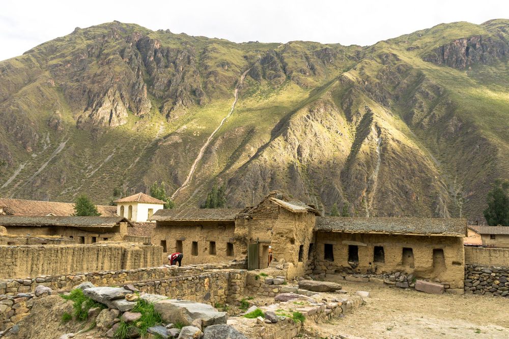Historic ruins of stone buildings stand along a mountainous valley trail in Peru, part of the ancient Inca Empire.