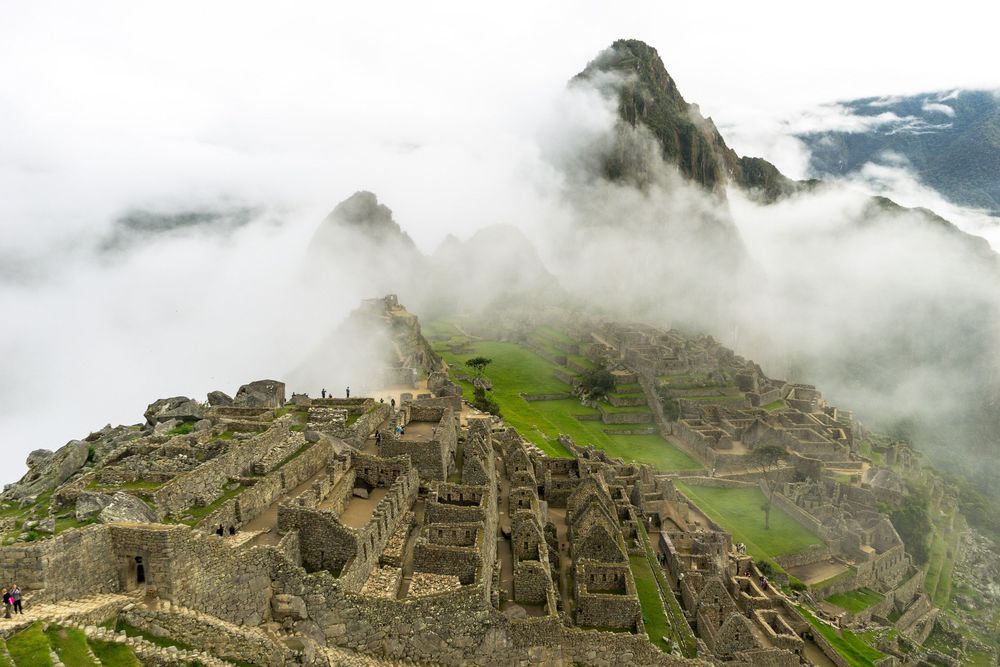Aerial view of the ancient Machu Picchu ruins nestled in misty mountain peaks on a cloudy day.