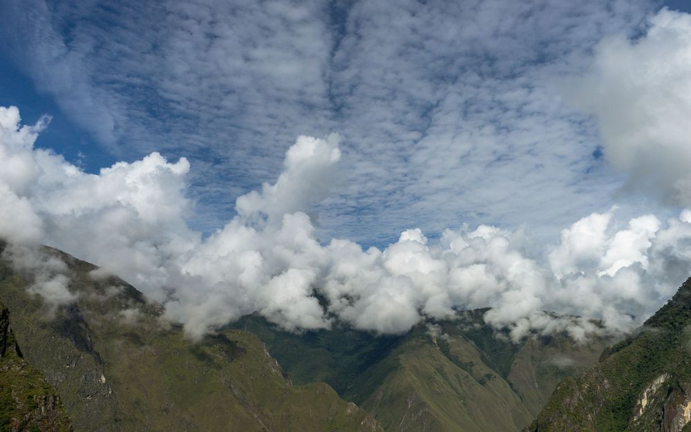 Panoramic mountain landscape with wispy clouds hovering over dramatic green peaks and valleys in tropical terrain.