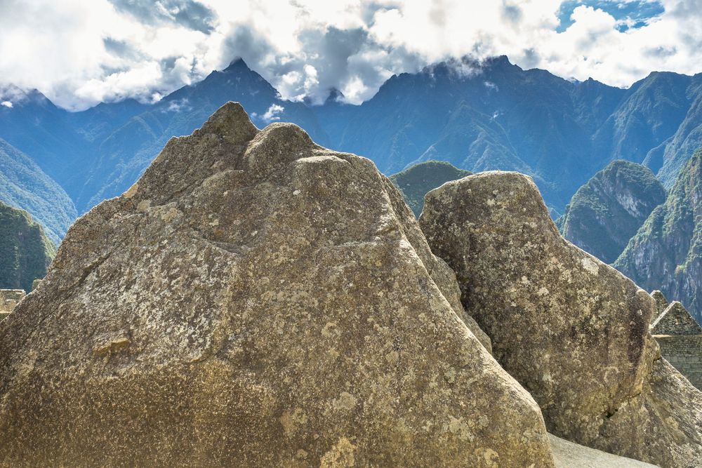 Panoramic view of rocky mountain peaks with snow patches under a cloudy blue sky in mountainous landscape.