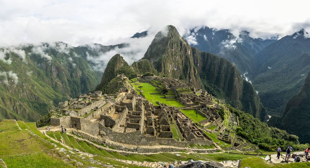 A panoramic view of ancient Machu Picchu ruins with surrounding misty mountains and green terraces in Peru.