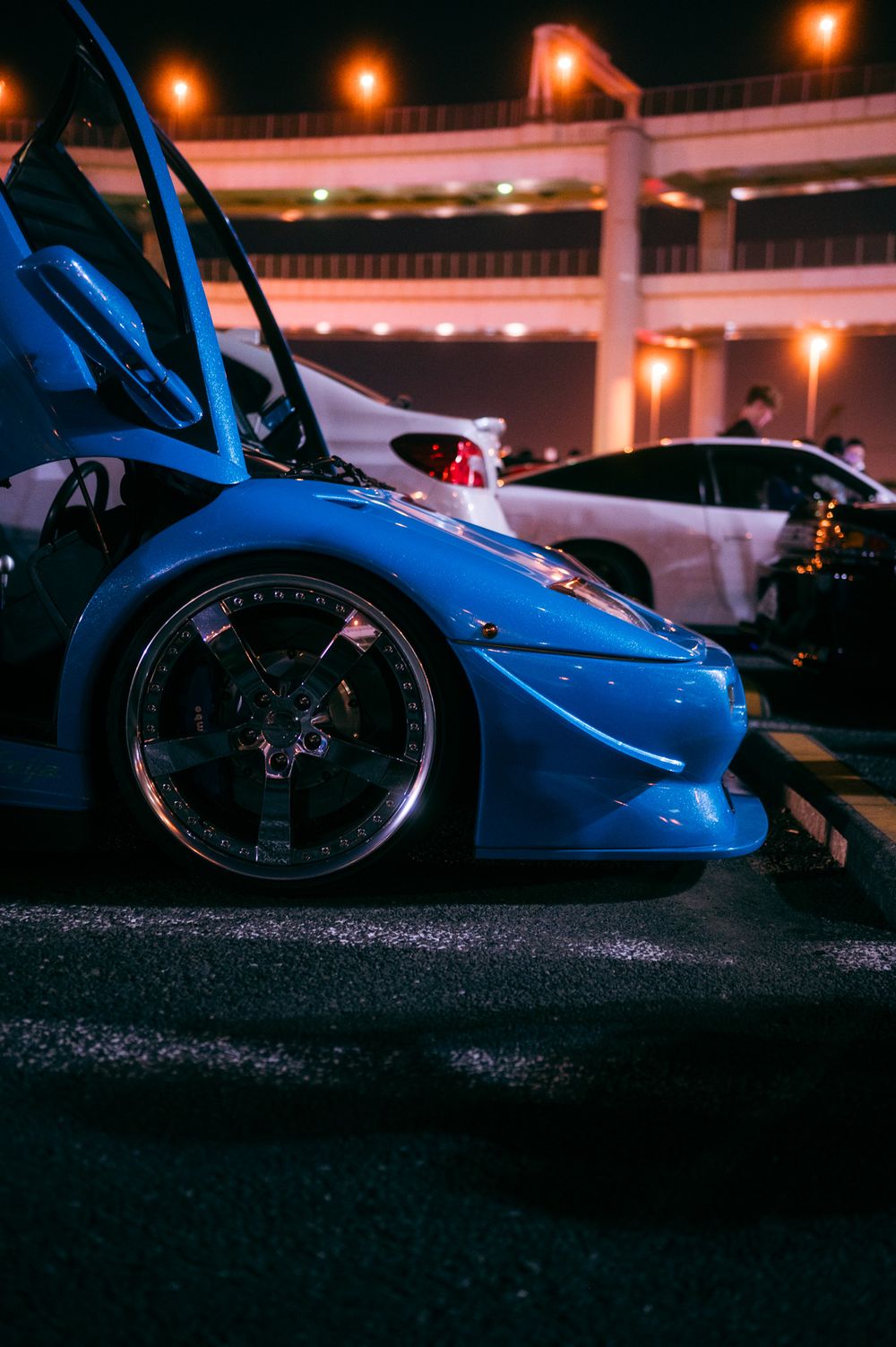 Low-angle silhouette shot of a sleek blue sports car under nighttime street lighting.