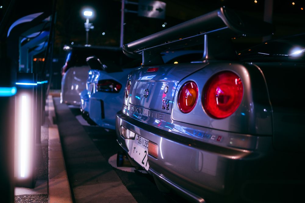Close-up view of a modified Nissan Skyline R34 GTR with red taillights glowing at night.