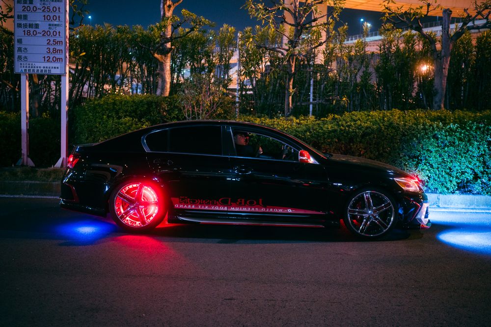 Black luxury sedan with custom LED underglow lighting and red wheel lights parked on dark street at night.