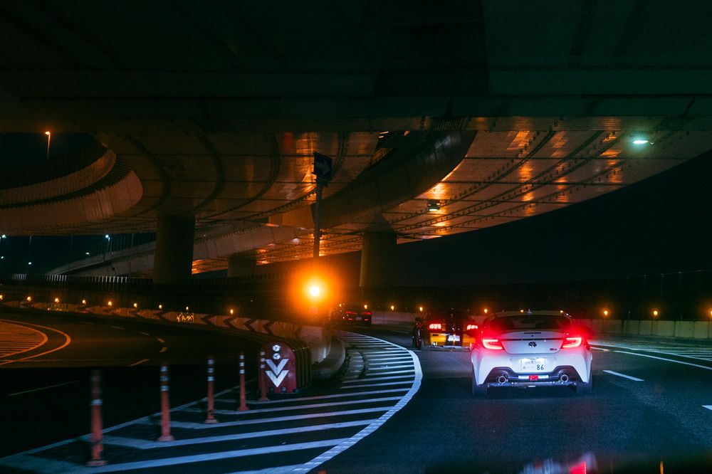 Dramatic nighttime highway scene with illuminated road barriers and red taillights streaking through the dark tunnel.