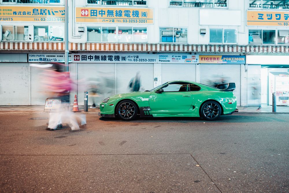 A bright green Porsche sports car parked at night under illuminated Chinese storefront signs in an urban setting.