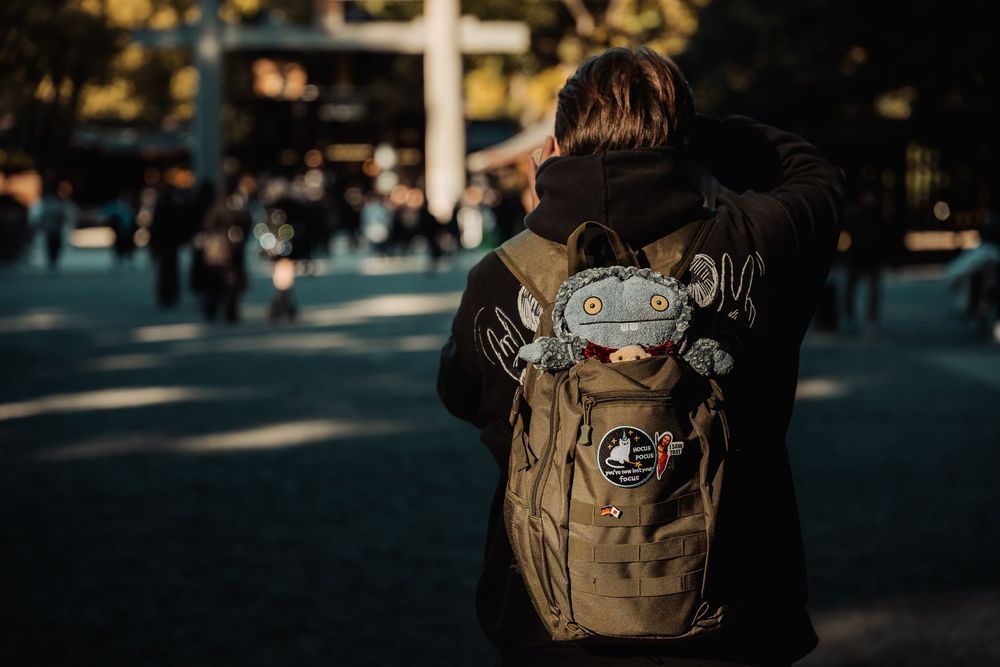 A row of students walking through a sunlit university campus walkway with backpacks and bags.