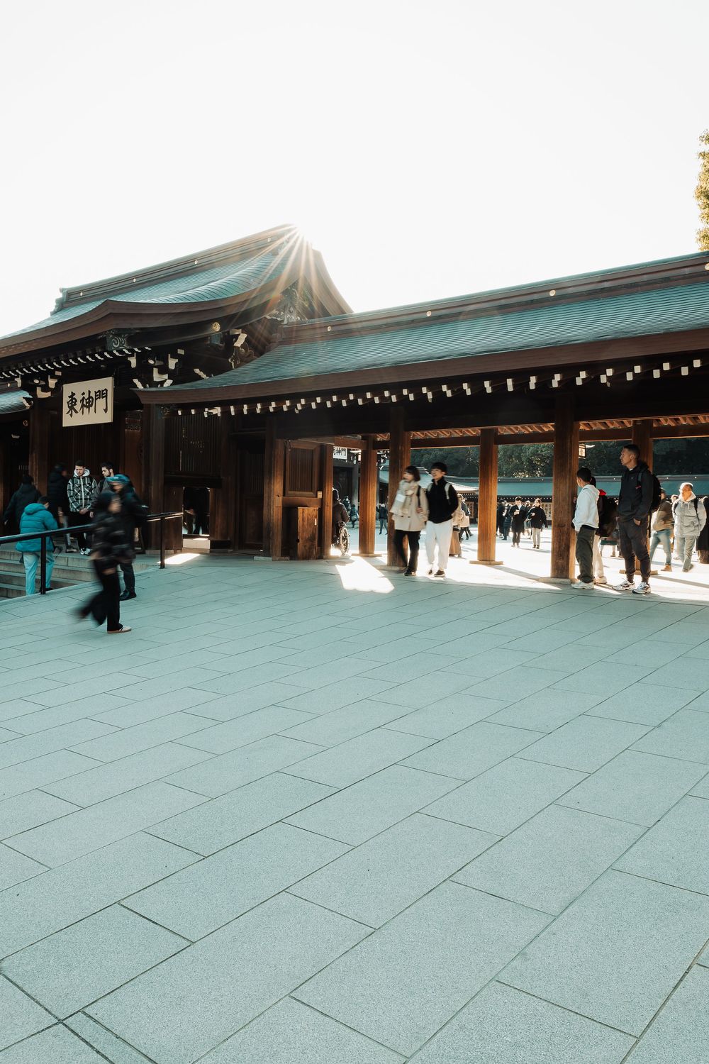 Traditional Japanese temple courtyard with stone pavement and wooden architecture under an overcast sky.