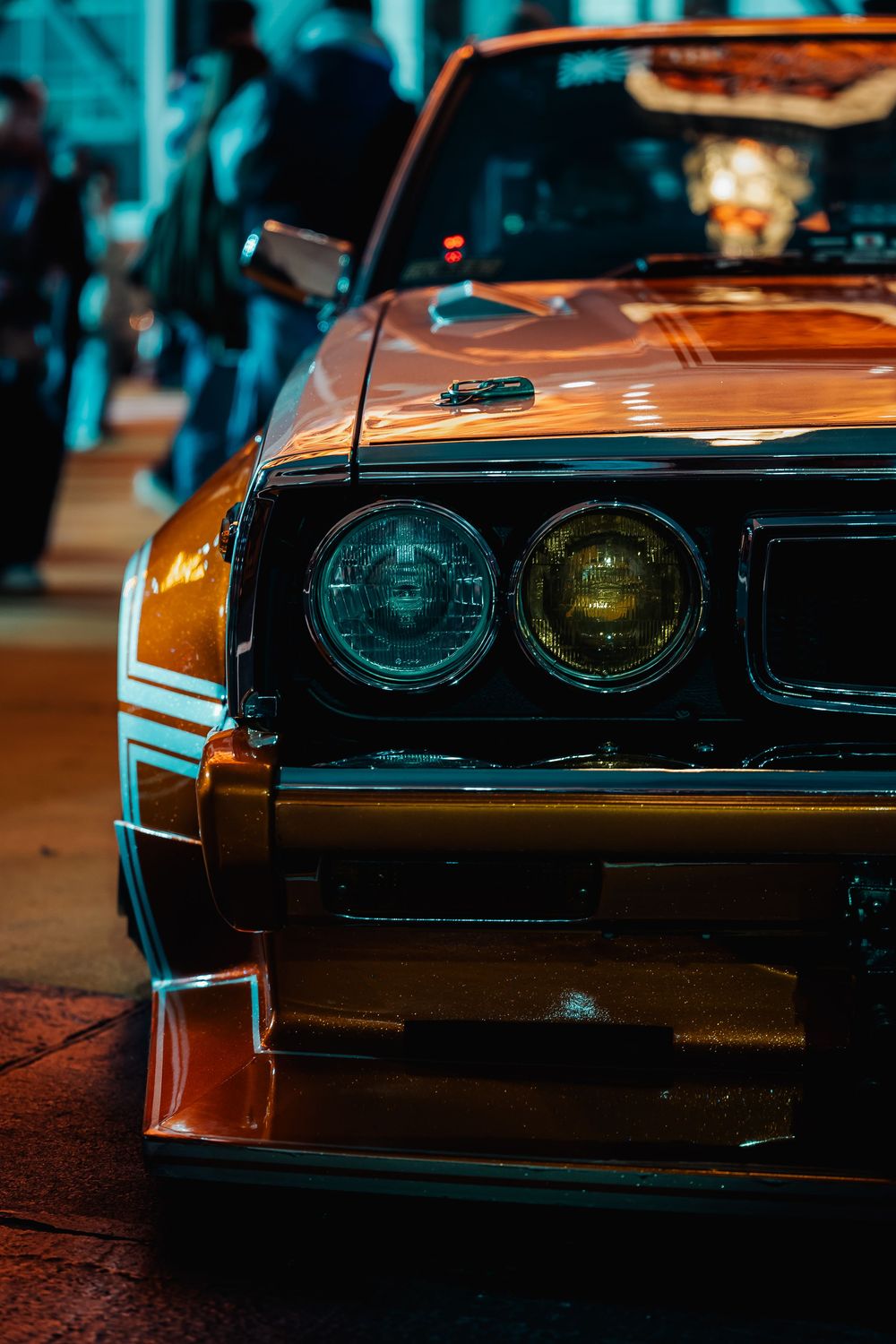 Close-up view of vintage muscle car headlights glowing with orange and teal lighting at night.