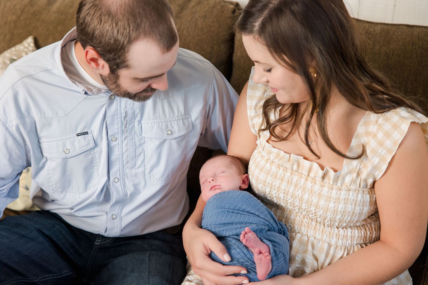 A couple holds their newborn baby while sitting on a blue and white striped blanket.