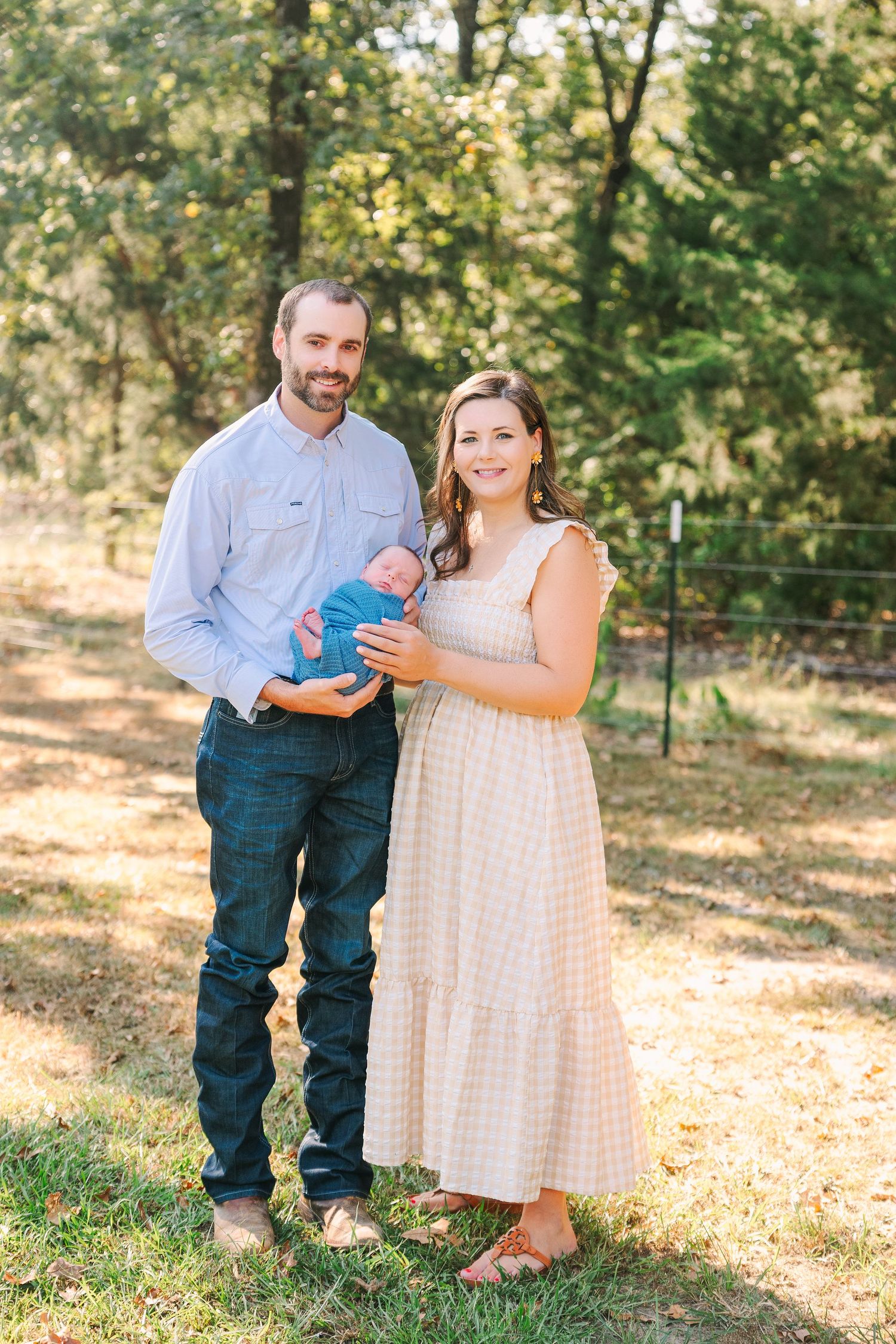 Gender reveal couple in casual outdoor setting hold up colored powder with excited expressions in a sun-dappled forest.