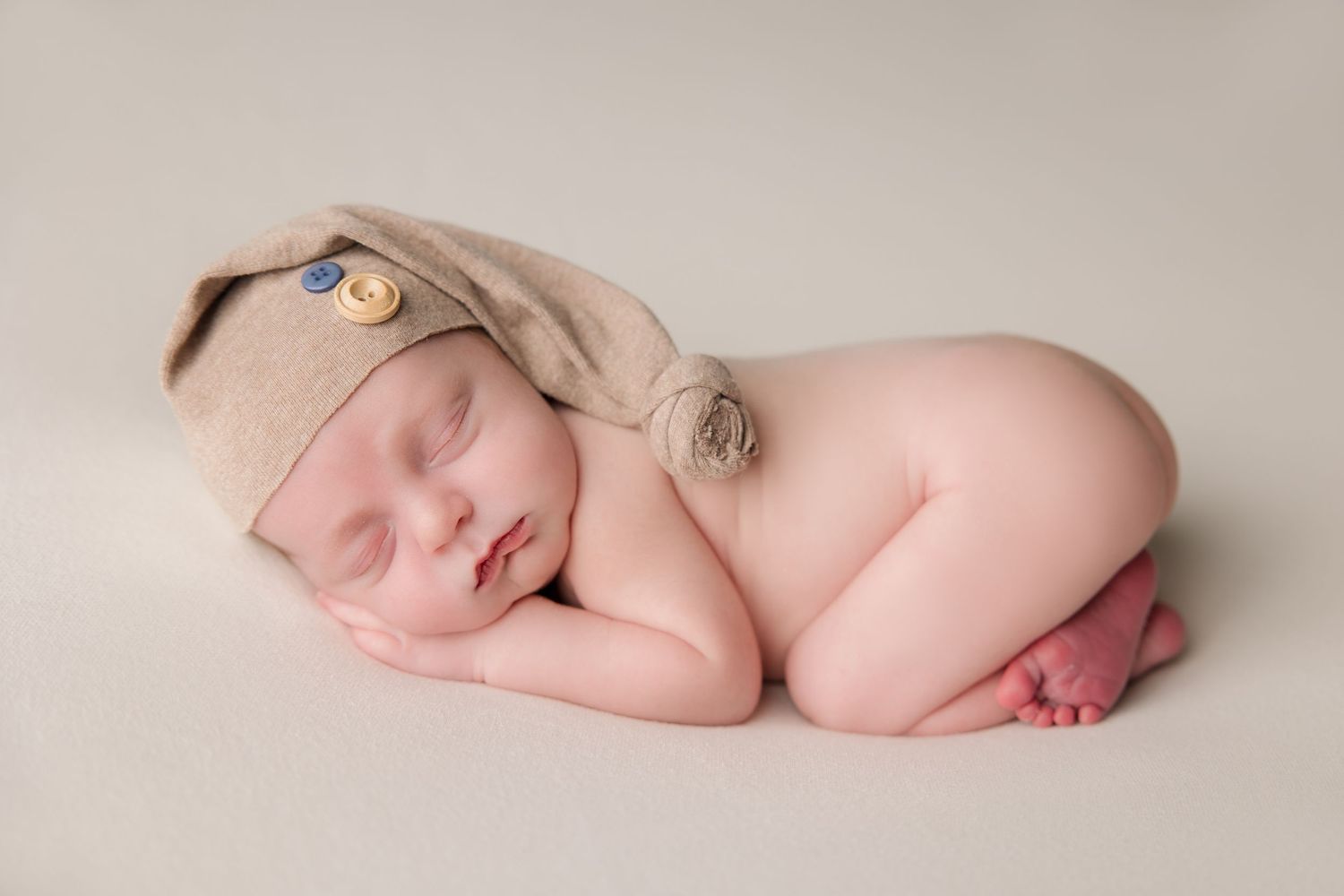 Newborn baby sleeping peacefully on soft beige backdrop during professional photo session.