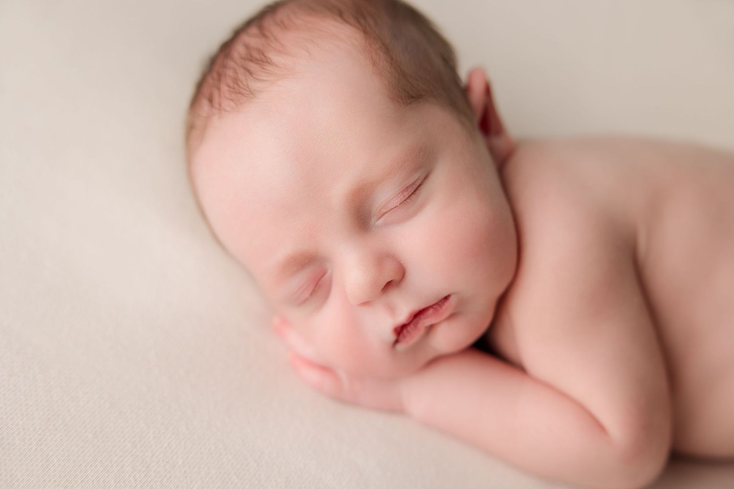 Peaceful newborn baby sleeping on soft cream background with delicate lighting in professional portrait style.