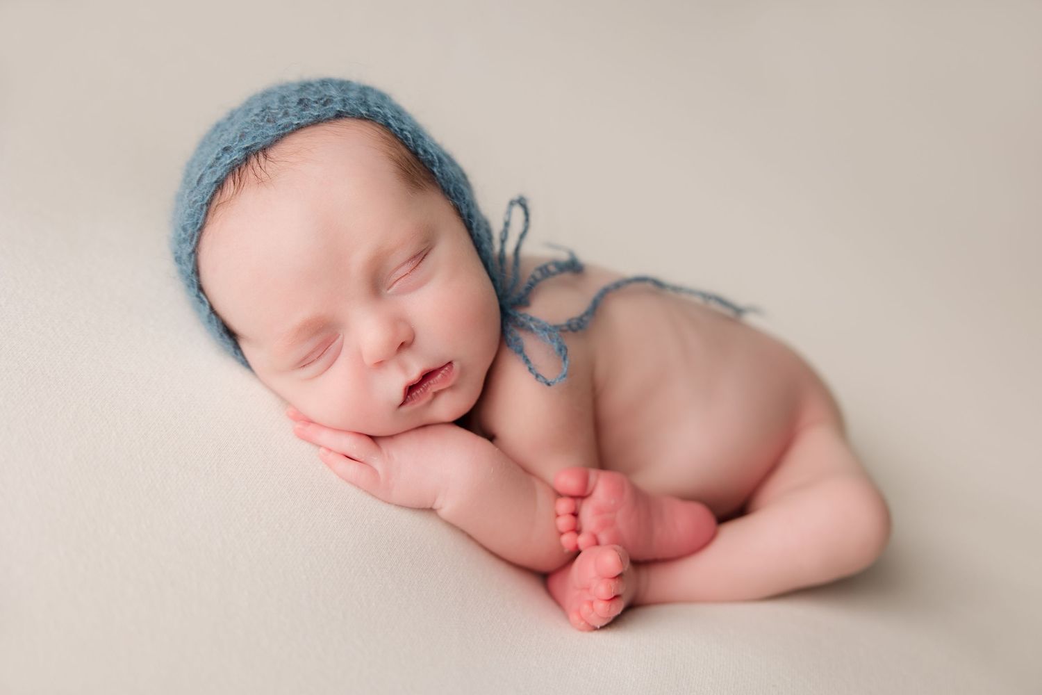 Series of minimalist newborn photos showing peaceful sleeping baby with blue textile accents on cream backdrop.