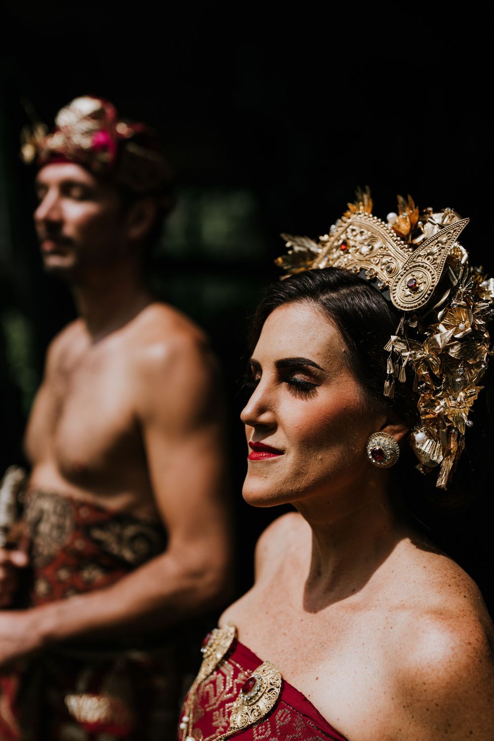 Dramatic side profile of bride wearing ornate gold Balinese headdress against dark background.