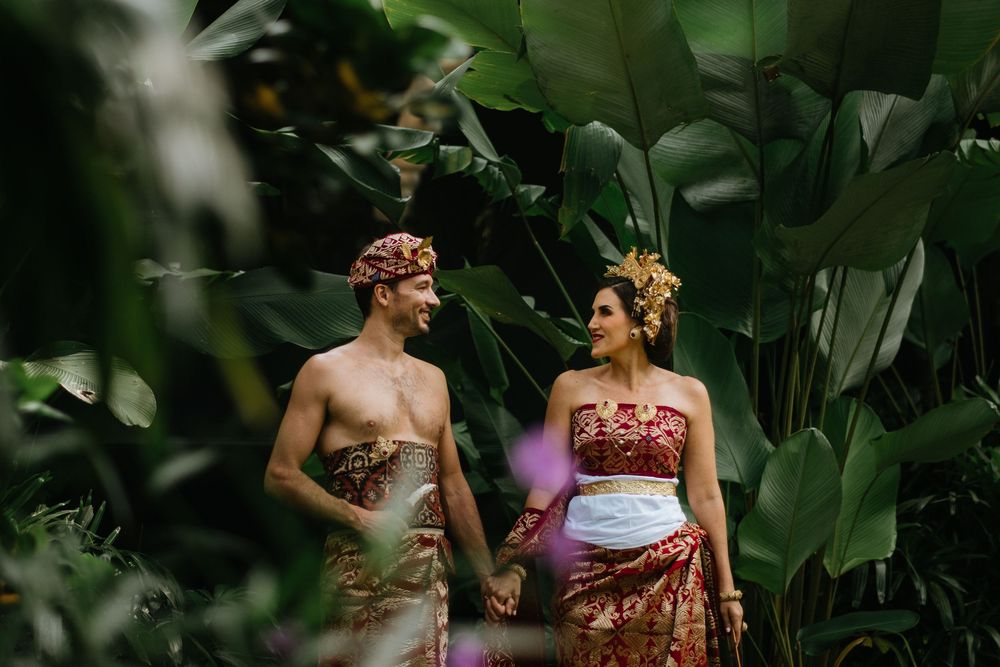Couple in traditional Balinese attire relaxing in a lush tropical garden setting.