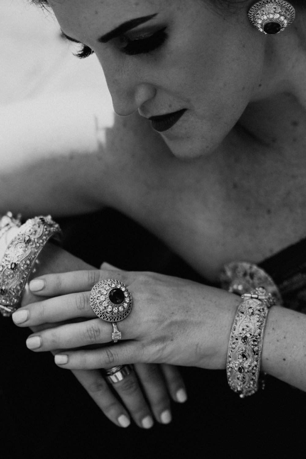 Close-up of ornate silver rings and jewelry on hands against dark background.