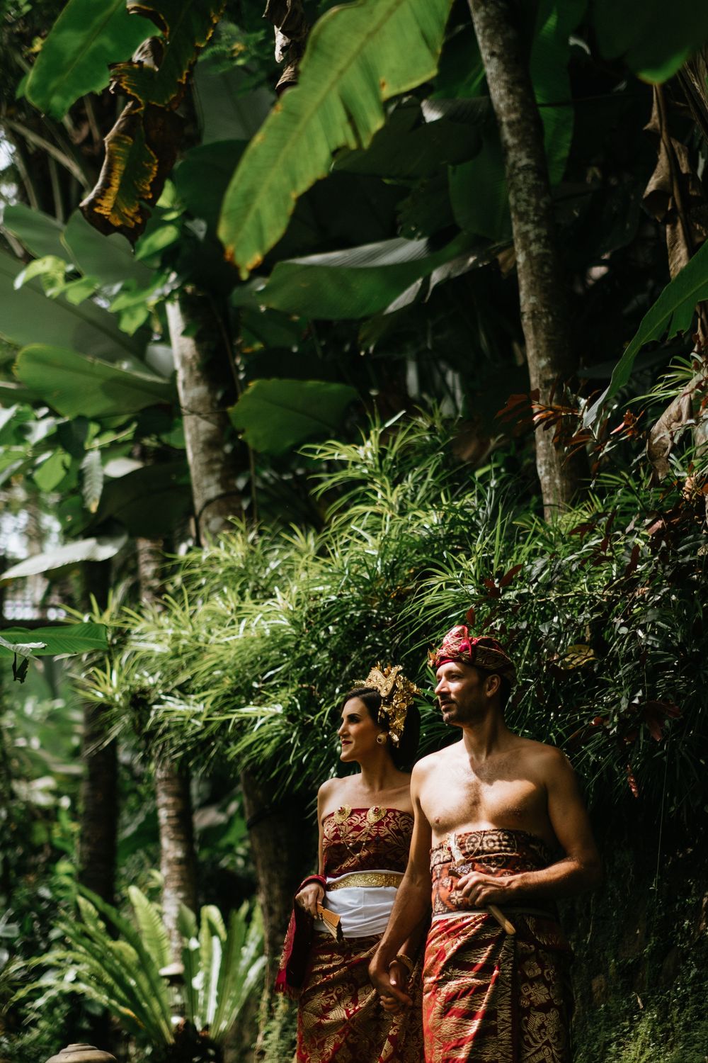 A romantic photoshoot in a tropical garden setting with traditional Balinese clothing and natural greenery.