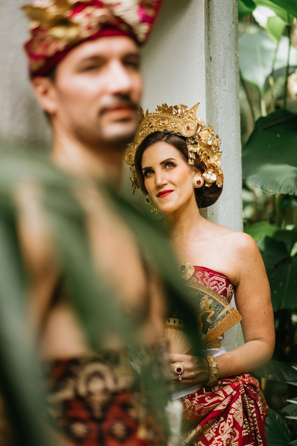 Romantic portrait through foliage of couple in traditional Balinese ceremonial dress.