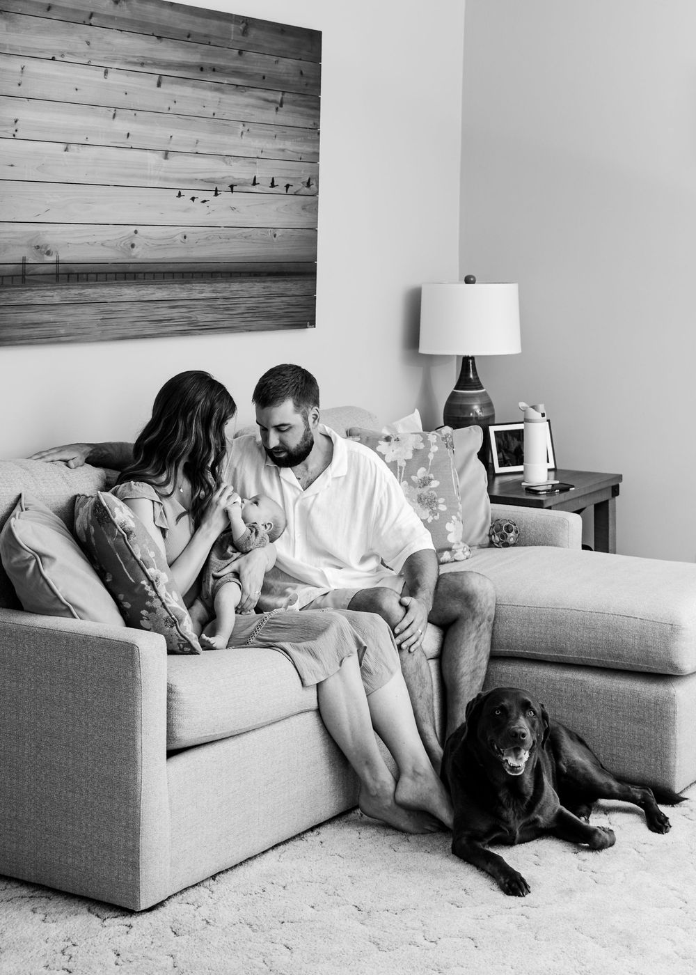 Family relaxing together on gray couch with their black dog.