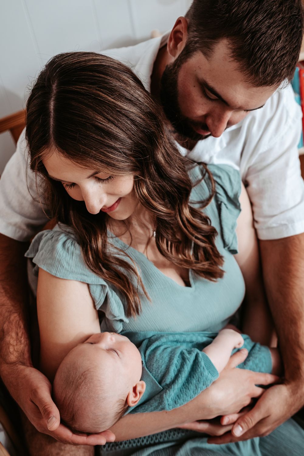 Parents in casual wear sharing tender moment with newborn baby on chair.