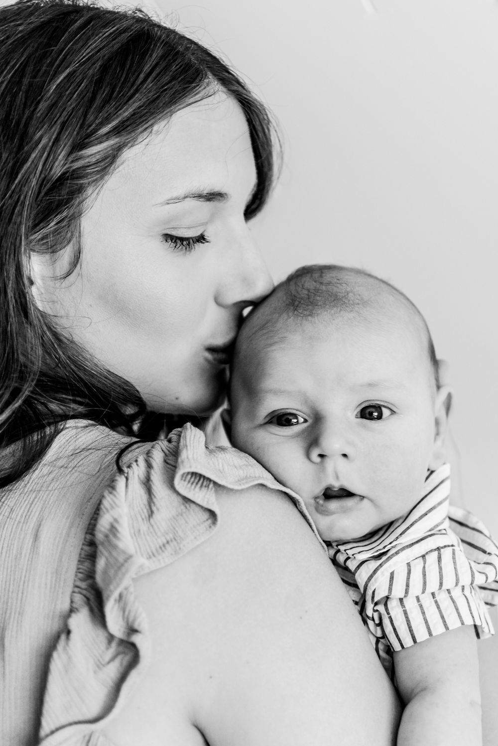 An intimate black and white portrait captures a tender moment between parent and young baby.