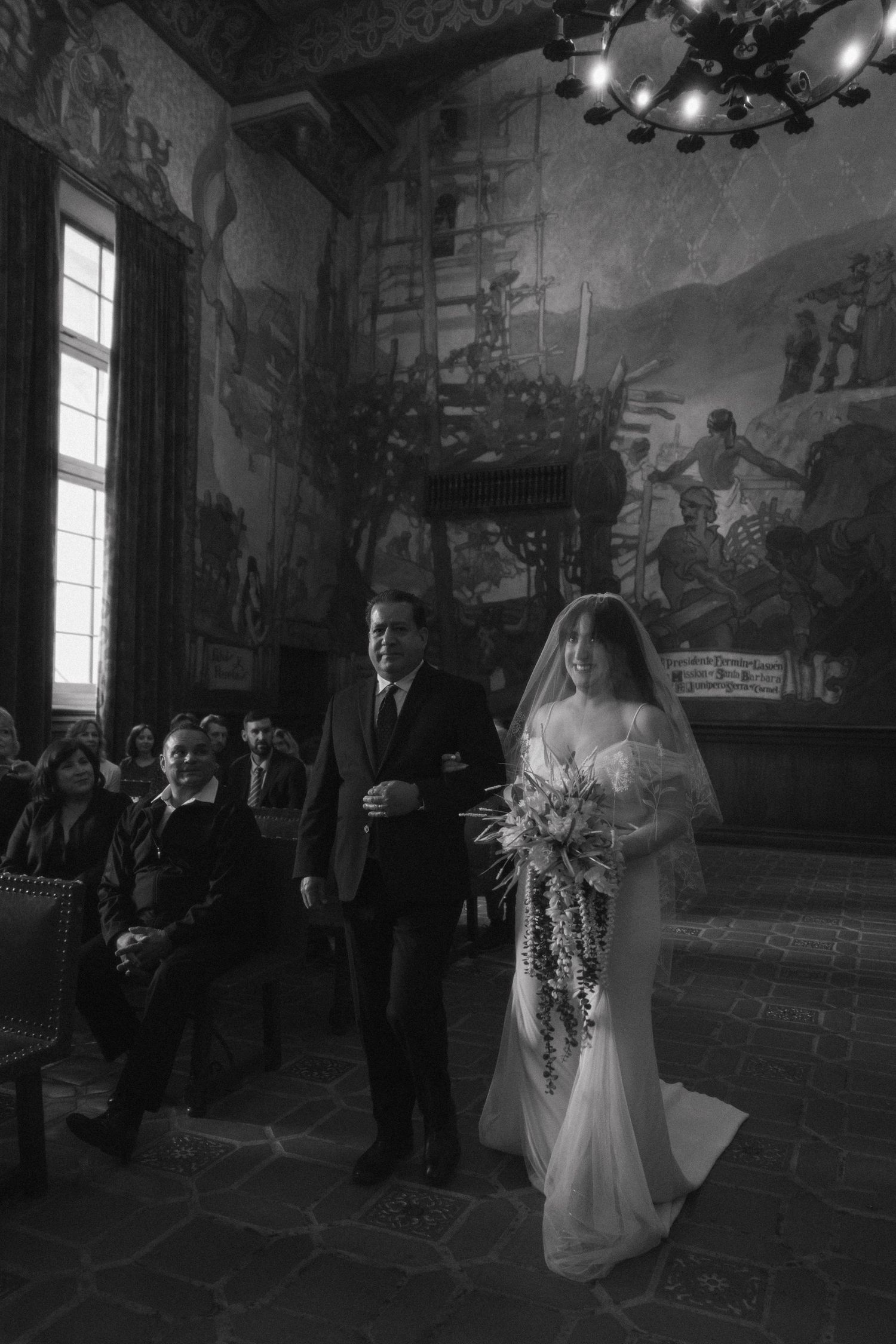 Black and white sequence of photos showing a wedding procession walking through an elegant hall with murals on the walls.