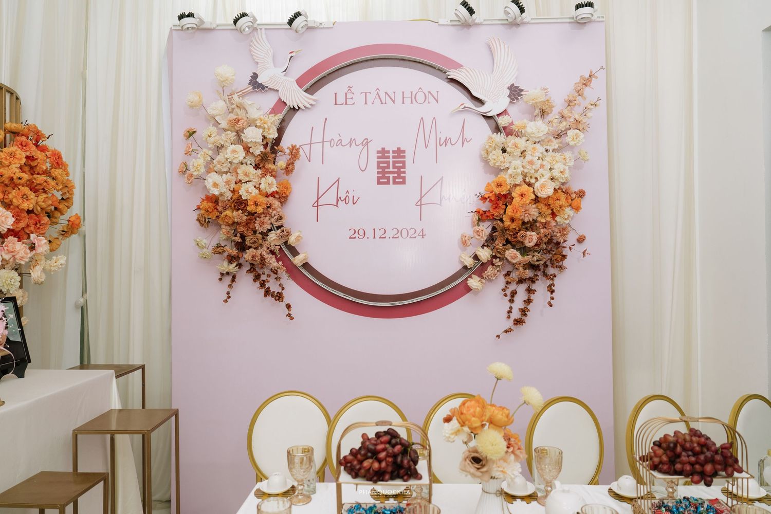 Vietnamese wedding reception backdrop with orange and pink floral arrangement and double happiness symbol dated 29.12.2024.