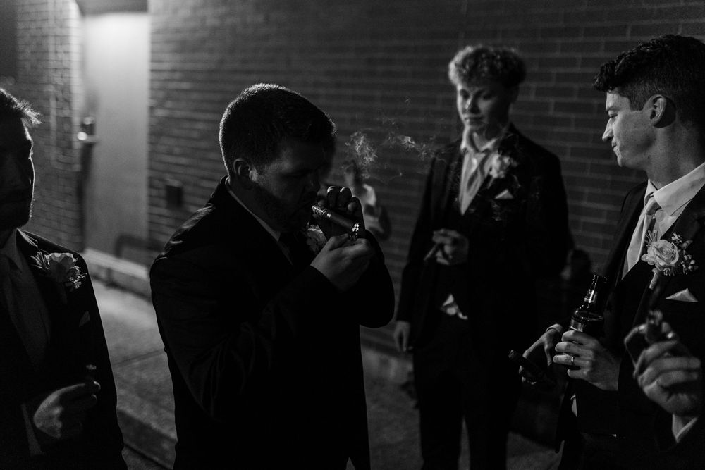 A group of students use mobile phones while standing in a dark hallway against a brick wall.