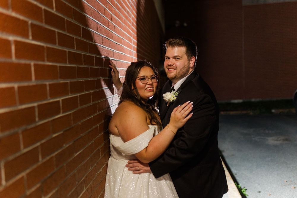 Wedding couple sharing romantic dance moments while embracing against red brick wall background.