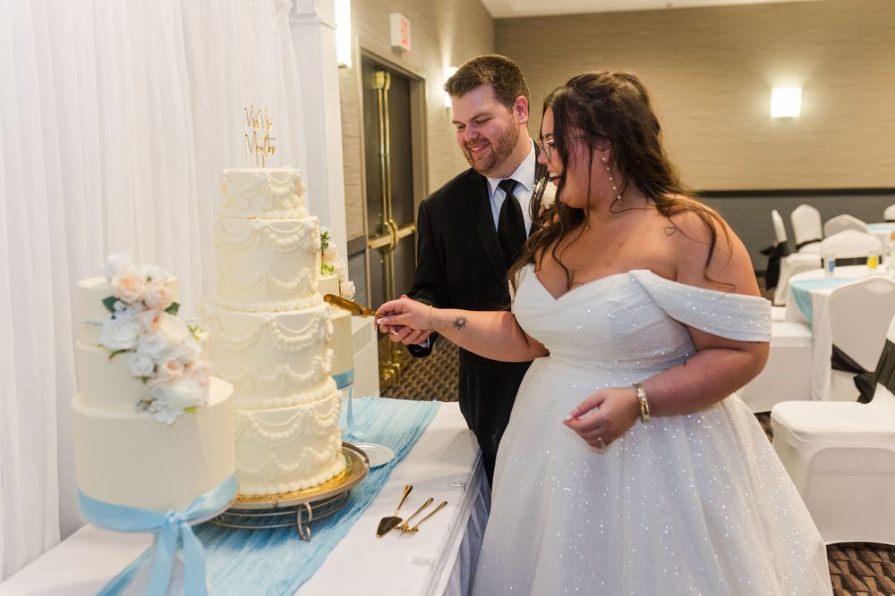 A couple cutting their elegant white wedding cake decorated with blue accents at their reception.