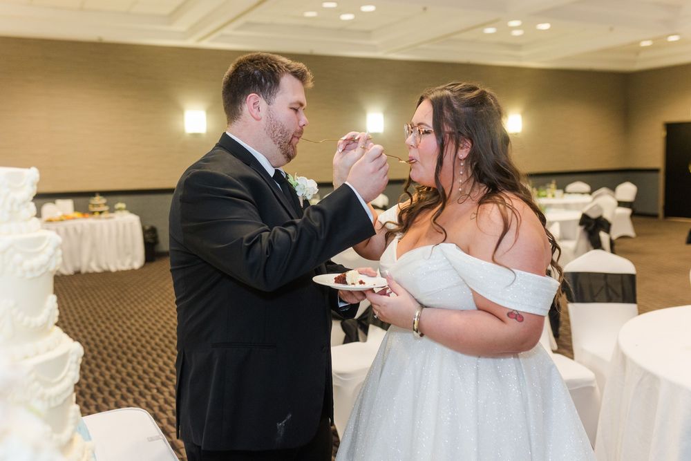 A couple at their wedding reception smears cake on each other's faces while sharing a playful moment in the banquet hall.