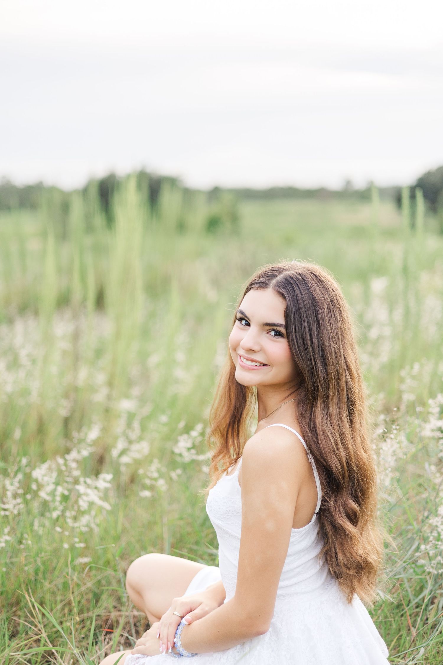 Woman in white dress sitting in a wildflower meadow on a bright summer day.
