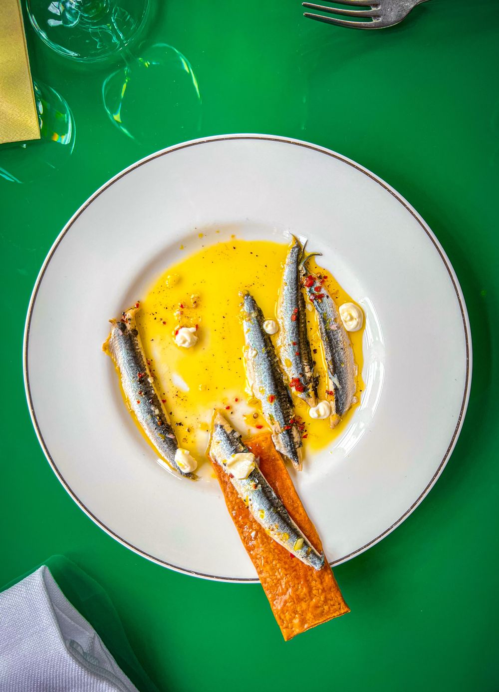 A served plate of grilled sardines garnished with citrus sauce and crispy orange slices on a vibrant green background.