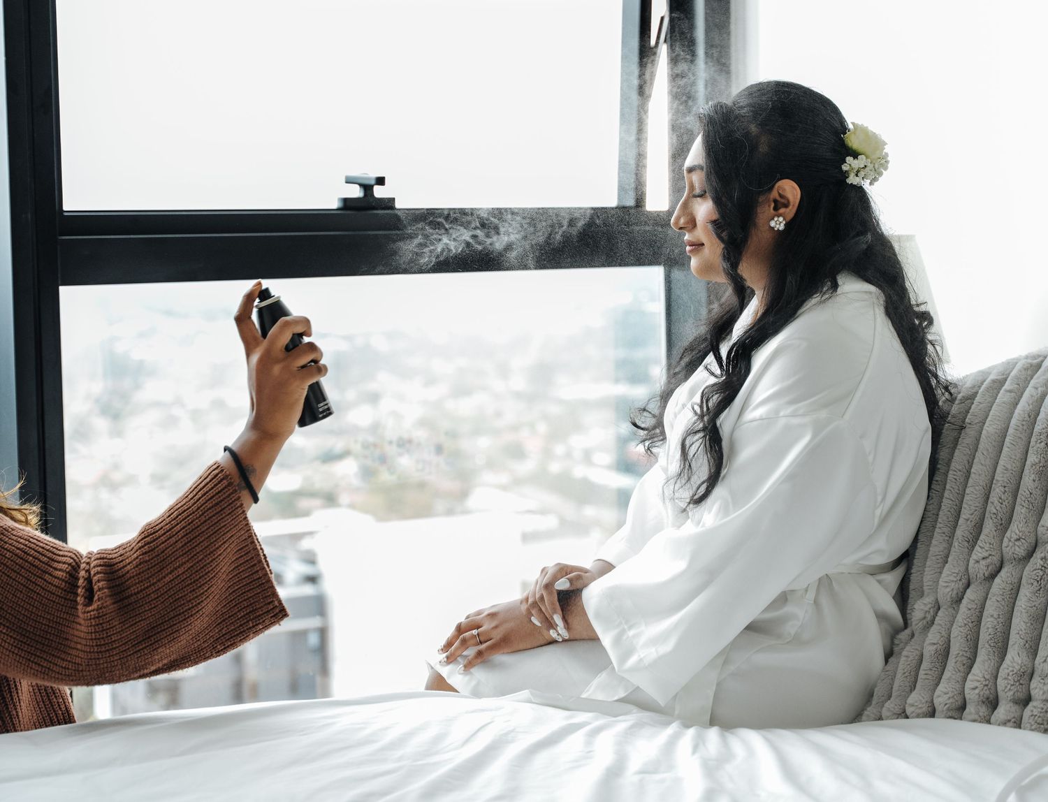 A person in a white bathrobe sits on a couch near a window while drinking from a coffee mug.