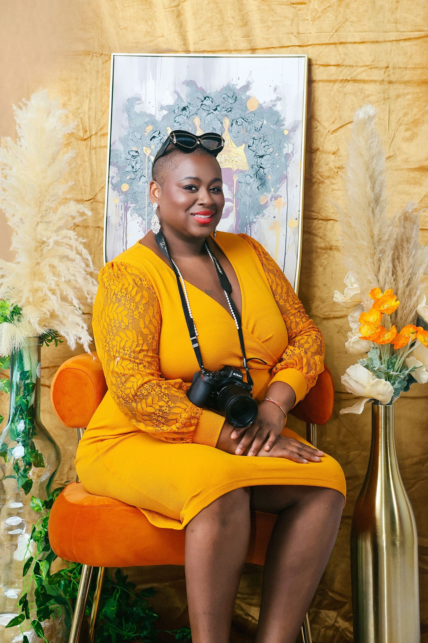 Zarinah Tavares, CEO/ Creative  in a bright yellow dress poses elegantly in a series of photos with floral decorations and golden backdrop.