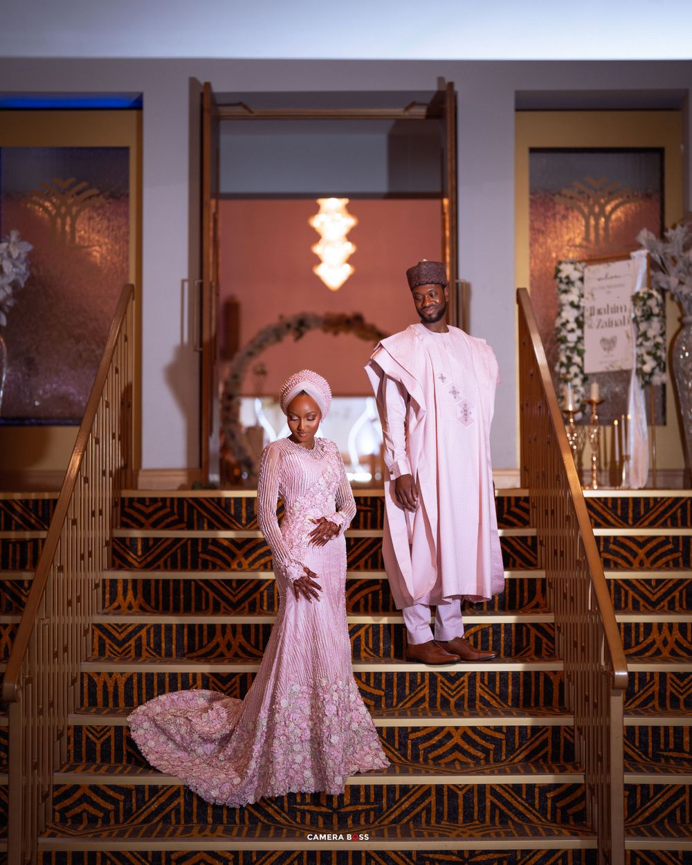 A couple in coordinated pink attire pose on a rustic wooden balcony with romantic lighting.