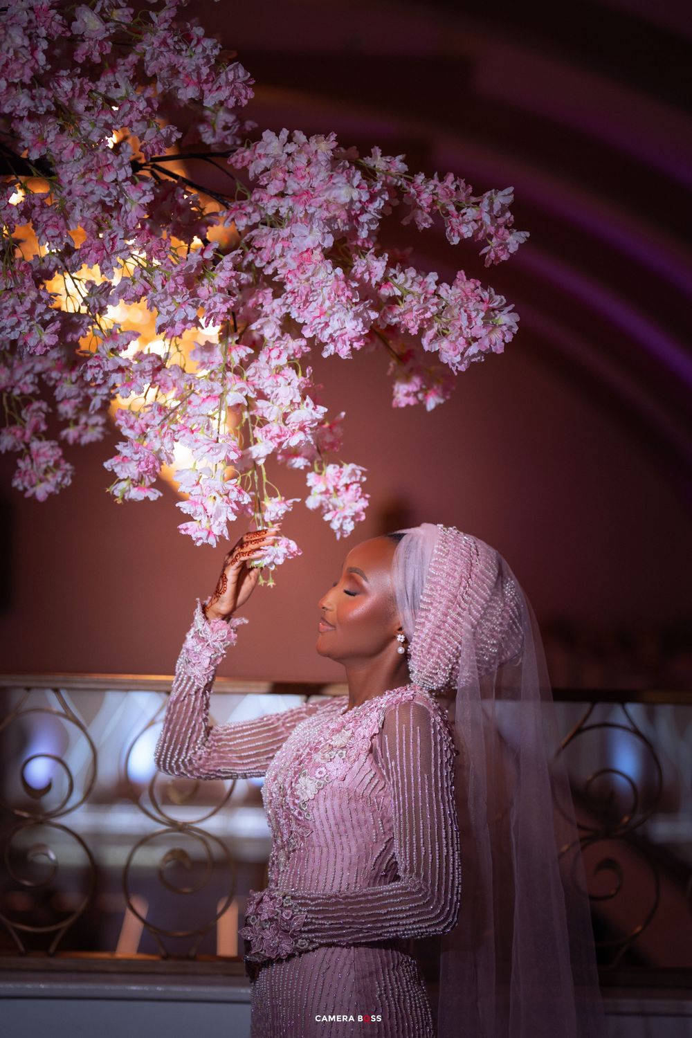 A dreamy bridal portrait under pink cherry blossoms with ambient lighting.