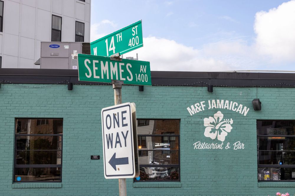 A street sign for Semmes Ave intersects with a teal-colored building featuring a Jamaican restaurant storefront.