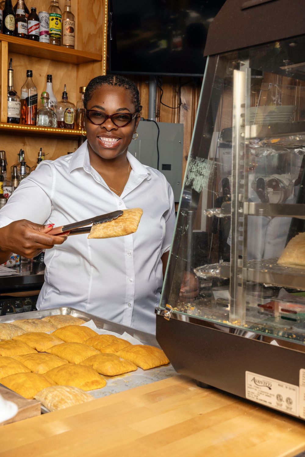 A pastry chef in white uniform works at a bakery counter preparing golden baked goods on a wooden surface.