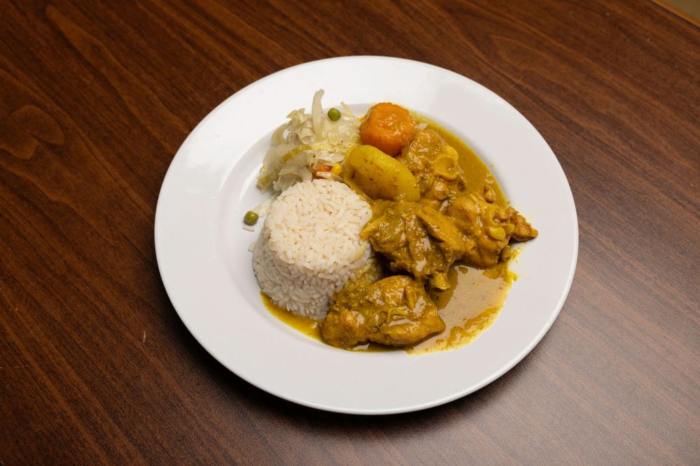 A plate of curry chicken served with white rice and a side of fresh coleslaw on a wooden table.