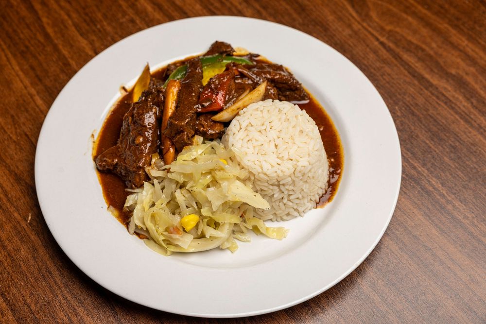Close-up of braised beef short ribs with mashed potatoes and cabbage in a dark rich sauce served on white plates.