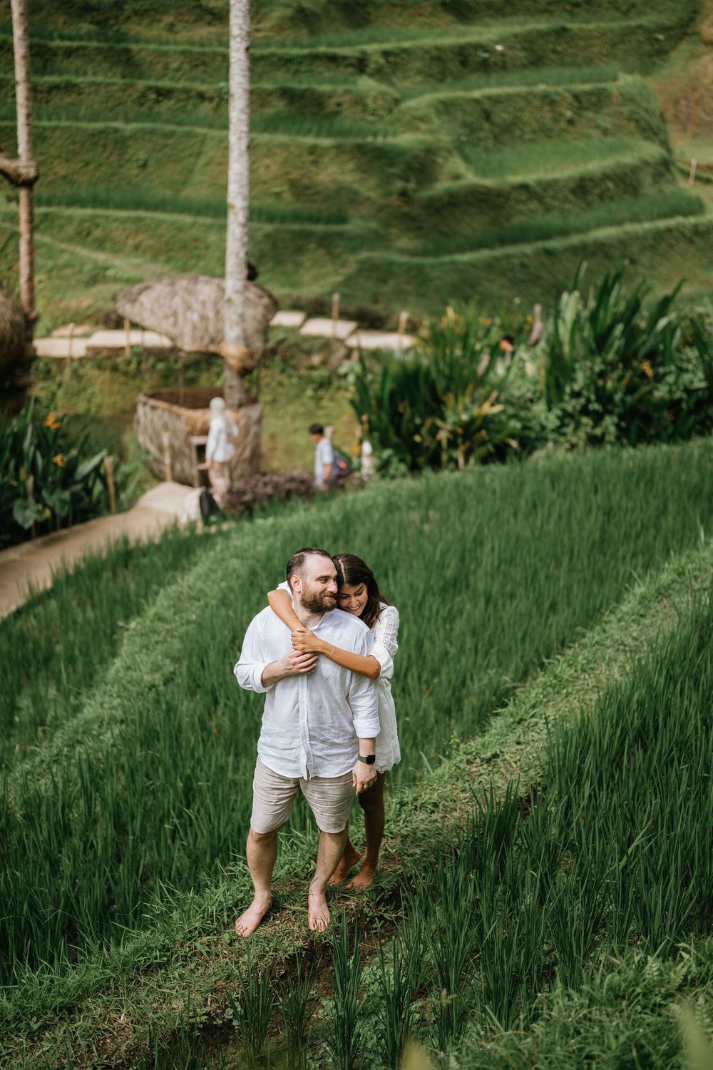 A couple in white outfits walking together through lush green terraced rice fields in Bali.