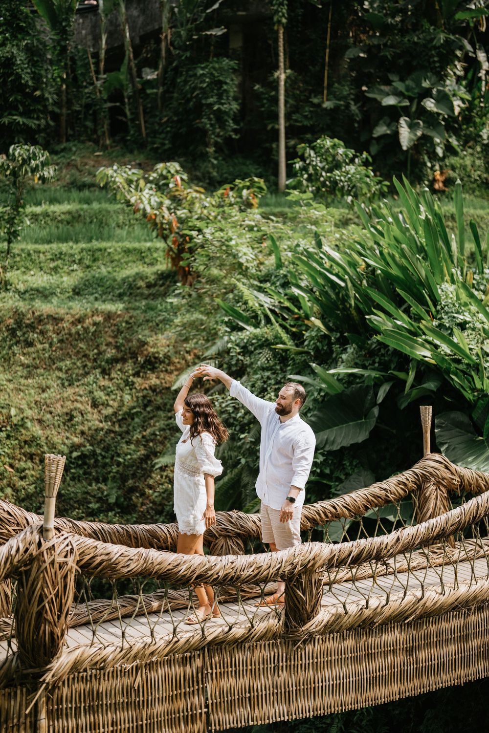 People walking along a rustic woven bamboo bridge surrounded by tropical foliage.