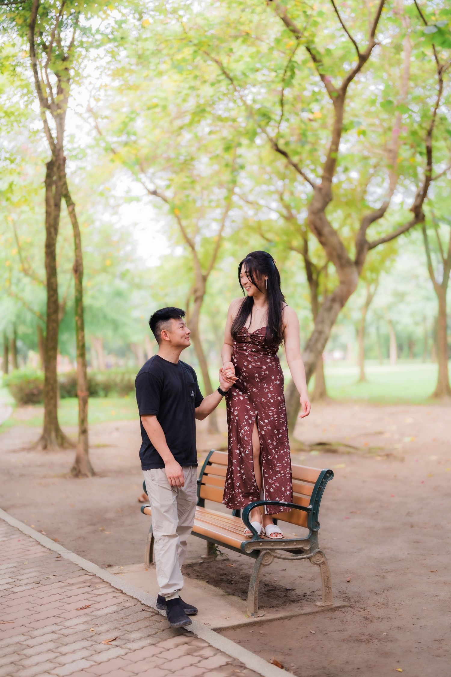 A couple shares a tender moment while sitting together on a park bench surrounded by trees in a natural setting.