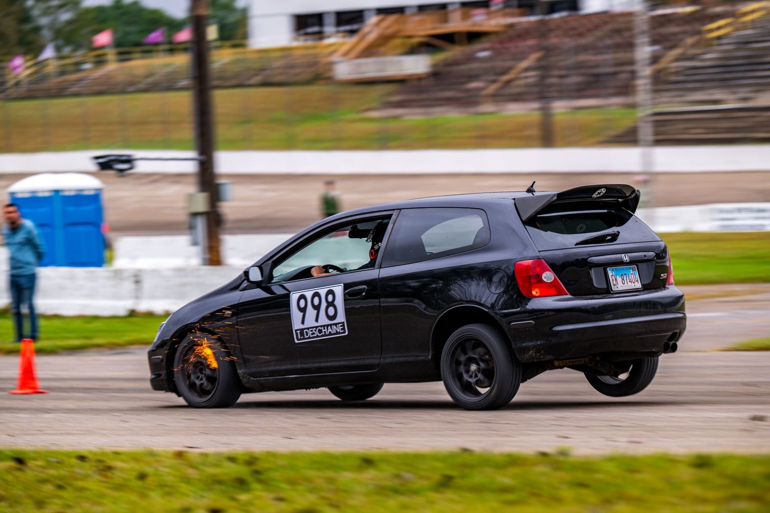 Black Honda Civic hatchback #998 competing in autocross race, navigating tight course with orange cones on pavement.