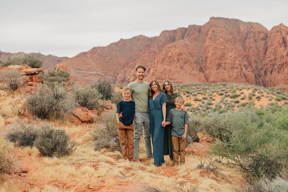 Family of five smiling together in a red rock desert landscape with scrubby vegetation.