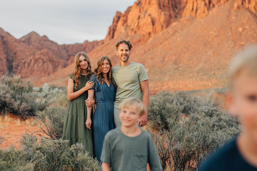 Family portrait with two women and a man posing in a scenic red rock desert with children in foreground.