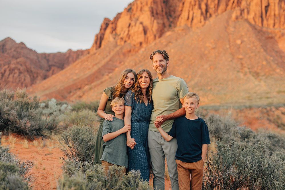 Happy family of five smiling together in golden hour desert red rock landscape.