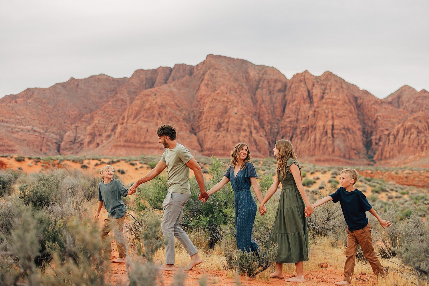 Family holding hands walking through red rock desert landscape with stunning sandstone cliffs in background.